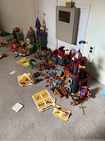 Wide view of Imaginext castles, figures, manuals, and assorted toy pieces arranged on carpeted floor.
