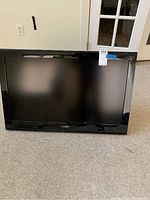 Front view of the Coby 37-inch TV powered off, showing the screen and bezel on a carpeted floor.