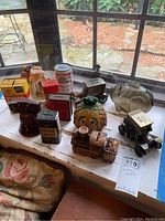 Overview of collection showing multiple vintage banks made of metal, glass, and resin arranged on window ledge with outdoor view.