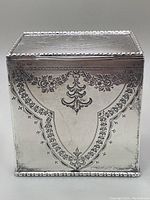 Front view of rectangular silver caddy showing chased floral swag pattern and beaded border on lid and base