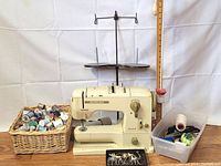 Full view of Bernina Record 730 sewing machine with basket of assorted thread spools, small container with sewing tools and presser feet tray
