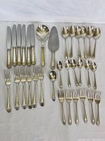 Six dinner knives, serving ladle, cake server and six tablespoons arranged on white cloth
