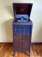 The floor standing gramophone with lid open showing the turntable and tonearm, wooden cabinet with decorative grille front.