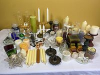 Table display of assorted candles, candle holders, and stained glass tealight holders arranged on a white surface against a yellow background.