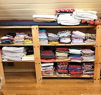 Wide view of wooden shelves stacked with multiple folded fabrics including quilting cottons, upholstery fabric, and cotton cloths in assorted colors and patterns.