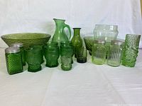 Front view of all green glass items showing bowls, pitchers, glasses, salt and pepper shakers, and the tall patterned vase.
