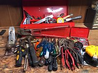 Collection of assorted hand tools including hammers, pliers, screwdrivers, snips, metal hand plane and yellow tape measure with red toolbox in background