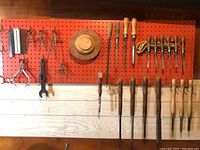 Full view of assorted hand tools mounted on orange pegboard and wood wall, showing two rows of tools including calipers, chisels, files, and measuring tools.