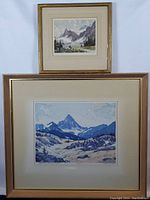 Two framed mountain scene prints, one larger and numbered, the other smaller with a lake scene.