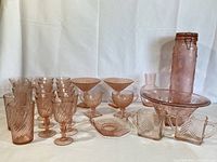 Front and side view of entire lot showing two rows of pink swirl wine glasses and tumblers, pedestal dish, creamer and sugar, covered jar, bowl and plate.