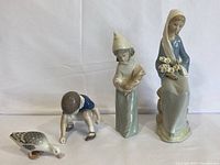 Overall view of the three porcelain figurines including boy with duck, girl with rooster, and girl with lilies.