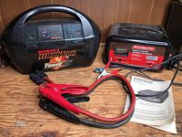 Overall view of Motomaster Eliminator Power Box and Motomaster Battery Charger with connecting cables and instruction paper on wooden surface.