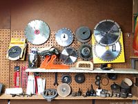 Photo of various circular saw blades, diamond sanding discs, and accessories mounted on pegboard and shelf.