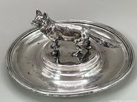 Side profile of fox figurine standing on circular silver dish, showing dish rim and figurine details