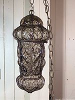 Side angle view of one pendant lantern showing glass texture and metal cage details along with hanging chain.