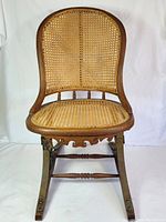 Front view of the vintage oak cane bouncer chair showing the woven cane backrest, seat and carved wooden frame.