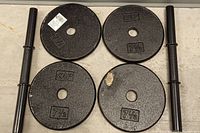 Four 7.5lb black iron weight plates arranged in a square with two black metal bar handles placed alongside.
