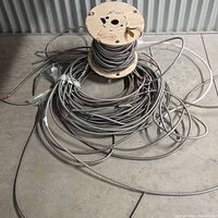 Wooden spool with approximately 60 feet of 14/2 BX armored electrical wire coiled around it, showing the spiral metallic armor covering.