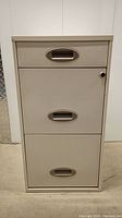 Front view of beige metal filing cabinet showing three drawers with metal handles and no lock.