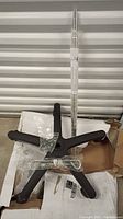 Foldable 5-leg black plastic wheeled base and aluminum adjustable pole standing upright inside a cardboard box with plastic wrap