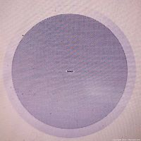 Close-up photo of the round white perforated grille of the ceiling subwoofer speaker, showing Tannoy logo at center.