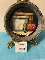 Front view of the circular hand painted metal plate resting on a gold decorative stand, showing the detailed apple, leaves, wooden board, and signature Phyllis.