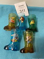 Set of five 1950s boot-shaped glasses in blue and green with colorful smoking themed decal graphics, arranged with a MaxSold lot number card.