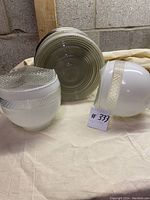 Three Art Deco light fixtures and shades placed on a beige cloth in front of cinder block wall, showing front and side views including textured frosted glass and decorative bands.