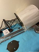 Photo showing the lamp shade wrapped in plastic, the metal arm, and mounting plate.