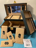 Open black and brown jewelry box showing inner compartments and included padded ring slots, divided trays, and mirror under lid along with four small suede-like pouches.