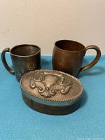 Front angle view of two cups and trinket box on blue surface.