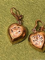 Close-up of earring front showing heart shape with clear faceted crystal center and gold-wash metal finish.