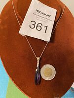 Sterling silver necklace with amethyst tear drop pendant placed on a brown velvet display with a coin for size reference.
