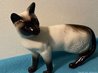 Front and side view of the porcelain Siamese cat figurine showing detailed facial features, body texture, and coloration.