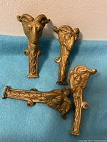 Four metal corner covers with detailed goat head designs arranged on blue fabric, showing intricate sculpting and antique finish.