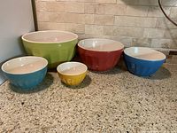 Five nesting bowls in primary colors arranged in a row on countertop.