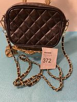 Front view of small black quilted leather cross body bag with gold and black chain strap hanging in front