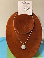 Front view of the necklace displayed on a brown velvet holder showing round moonstone pendant and silver snake chain.