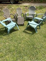 Six Adirondack chairs and one footstool arranged in a circle on grass. Colors visible: light blue, dark brown, and light gray.