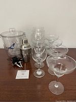 Front view of barware set on wooden surface including ice bucket, cocktail shaker, glasses, and bottle pourers