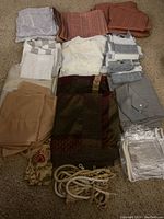 Top view of several folded drapes, sheers, tiebacks, and valances in various neutral and warm tones laid on carpeted floor.