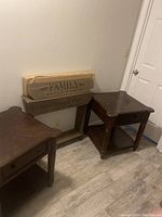 Two dark wood end tables with single drawers and lower shelves against a wall, taken from an angle showing tops and legs.