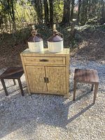Photo showing storage cabinet flanked by two small wooden end tables with two ceramic lamps on top, outdoors on gravel.