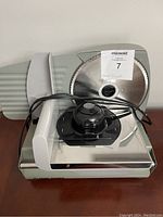 Front view of Game Winner electric meat slicer showing circular blade, sliding meat holder, and power cord.