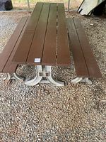 Top angle view of long 8ft brown wooden picnic table showing the tabletop consisting of 6 wooden planks and one adjacent bench with white metal legs on gravel ground.
