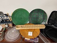 View of large serving platters including green ceramic and tartan pattern, glass platters, wooden lazy Susan, and wooden bread cutting board