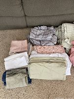 Queen bedding linens including fitted sheet, flat sheet, pillowcases, and dust ruffle arranged on floor