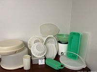 Photo of the Tupperware lot showing various plastic kitchen containers, bowls, a grain mill, grater and strainer in shades of white, beige, and green.