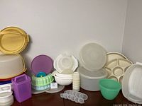 Wide view of assorted Tupperware items arranged on a surface including bowls, lids, bundt mold, divided tray, and multiple containers in various colors and sizes.