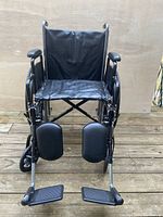 Front view of black wheelchair with elevating leg rests and padded footplates, showing seat, armrests and leg supports